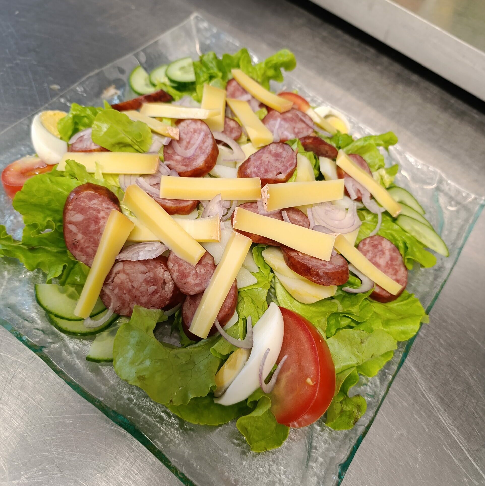 Salade verte, tomate, œuf dur, pomme de terre vapeur, saucisse fumée, échalotte, bâtonnets de Comté, sauce vinaigrette