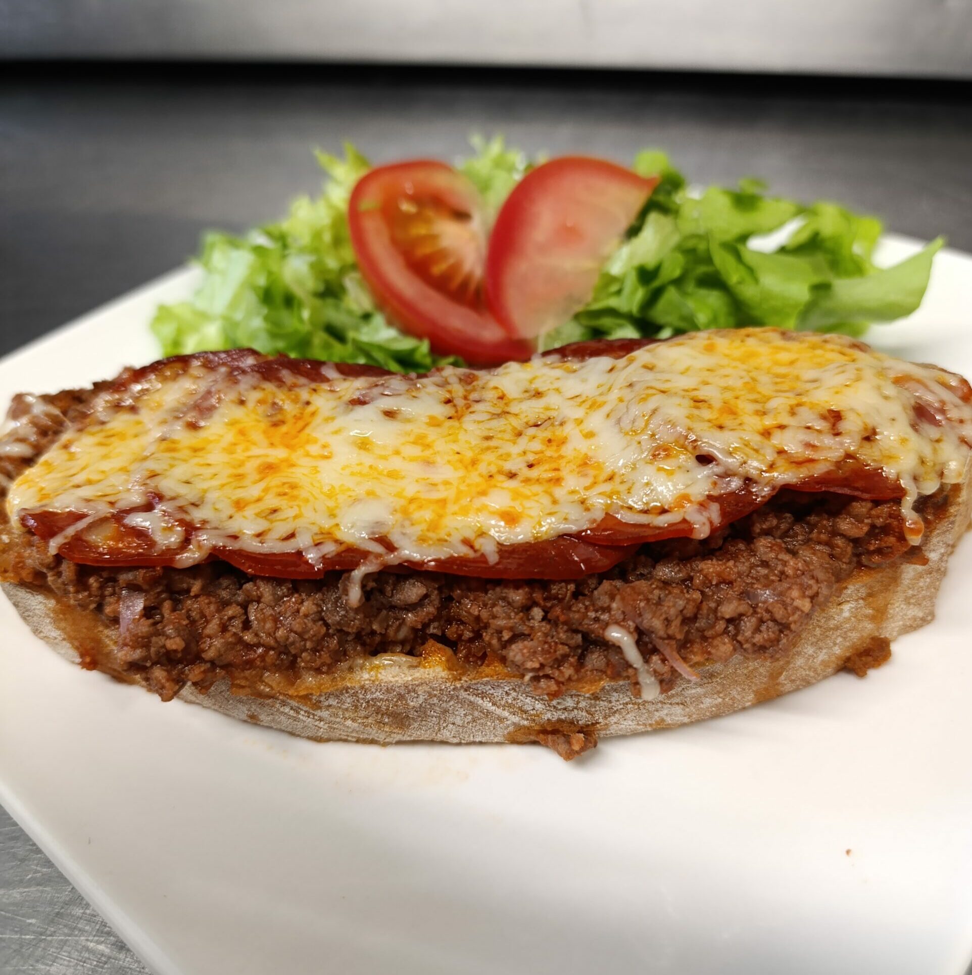 Tartine, viande de bœuf hachée, sauce tomate, chorizo, emmental râpé Accompagnée desalade
